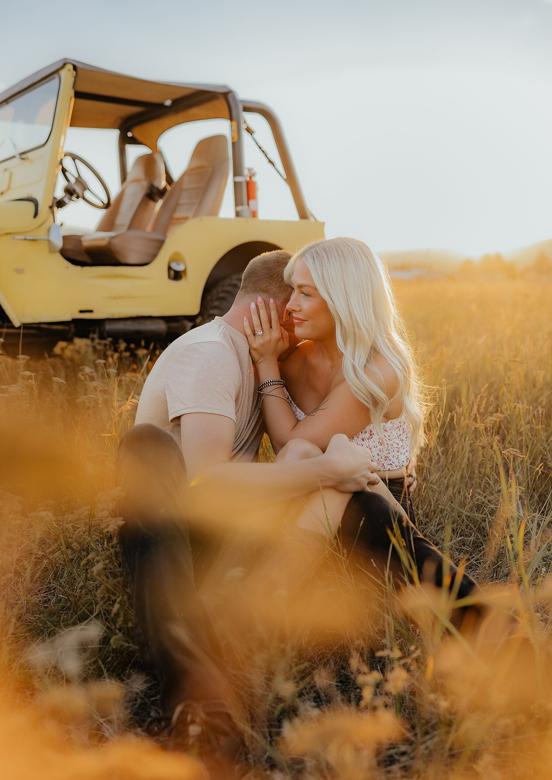 couple sit in golden field of grass in Montana during photoshoot