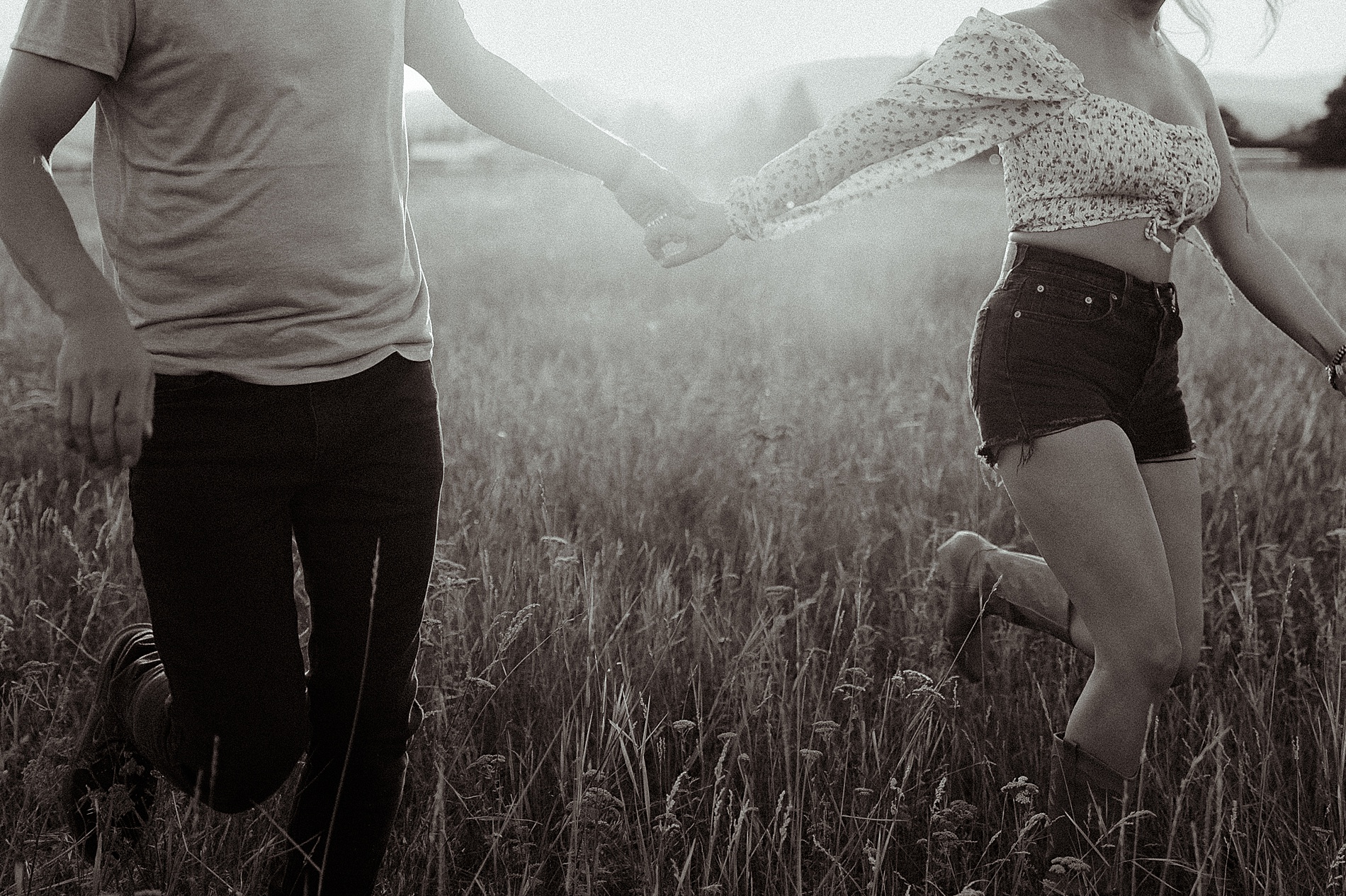 couple hold hands as they walk through field 