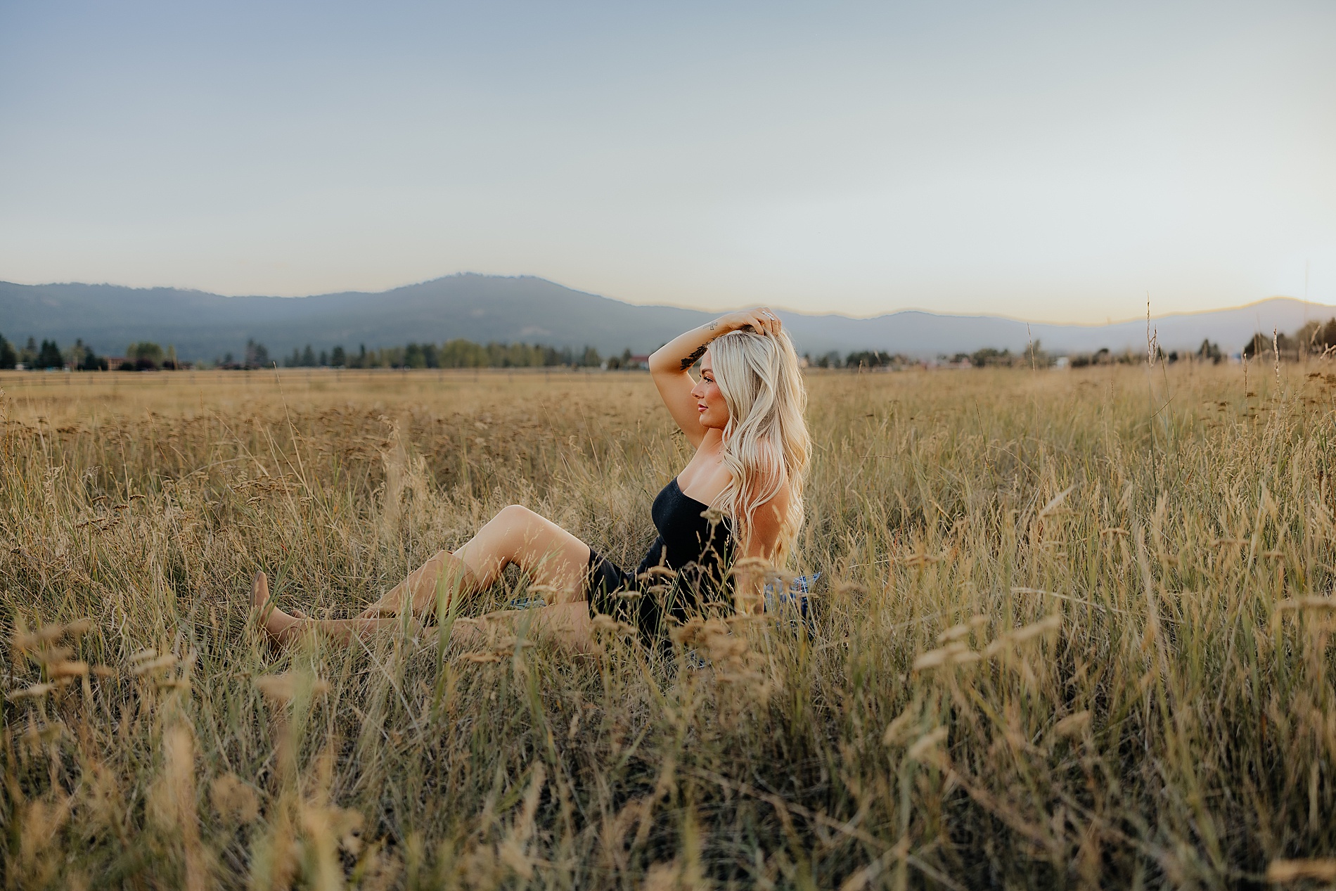 woman sits in field of tall grass with the mountains in the background