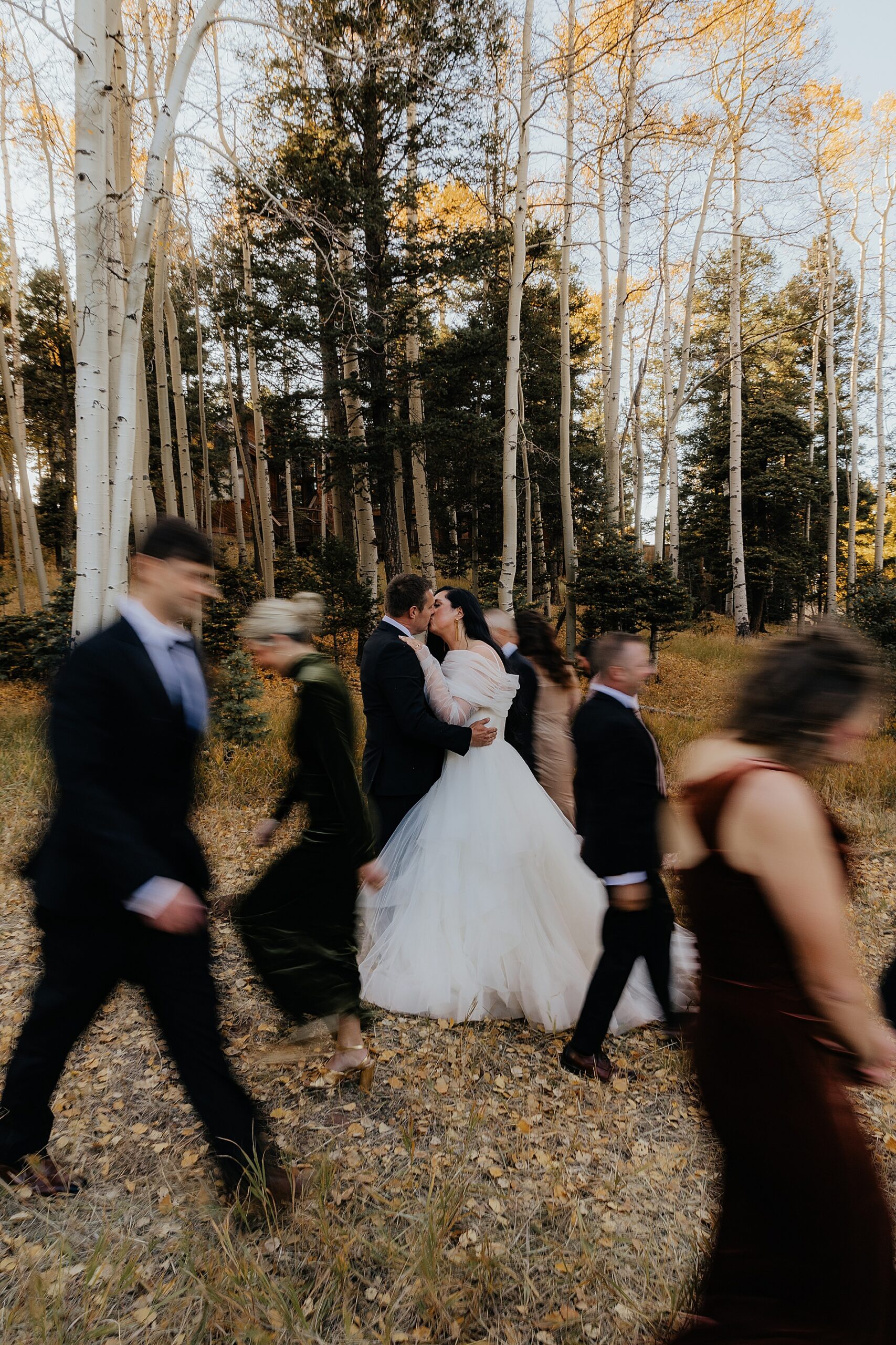 bride and groom kiss as wedding party walks around them 