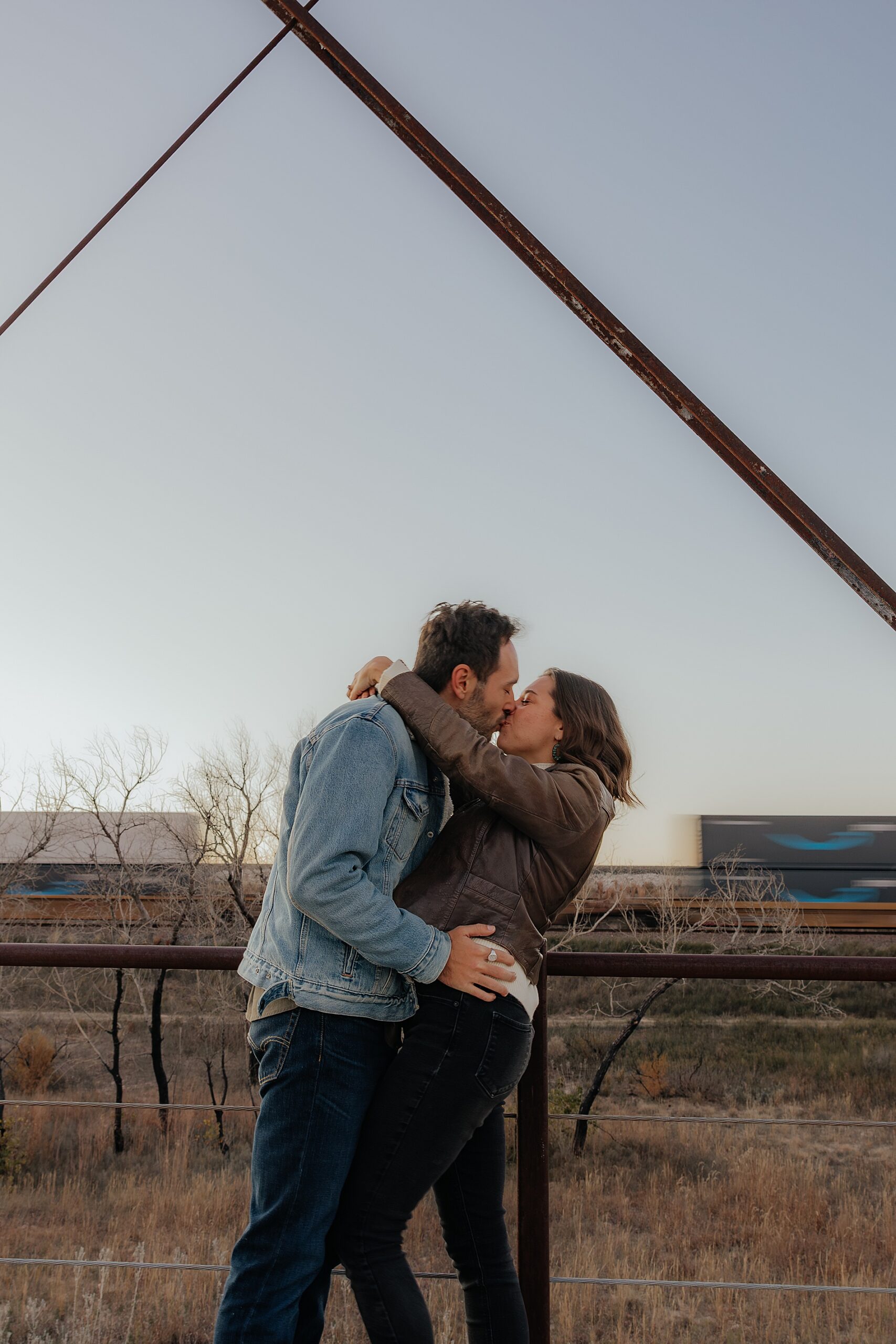 engaged couple kiss as train goes by at Canadian River Bridge