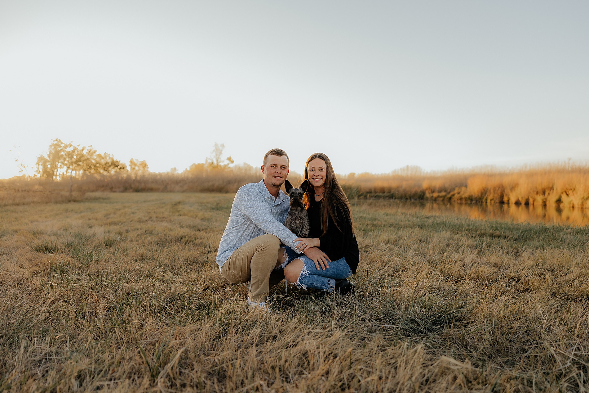 couple kneel down in field with their dog during engagement session