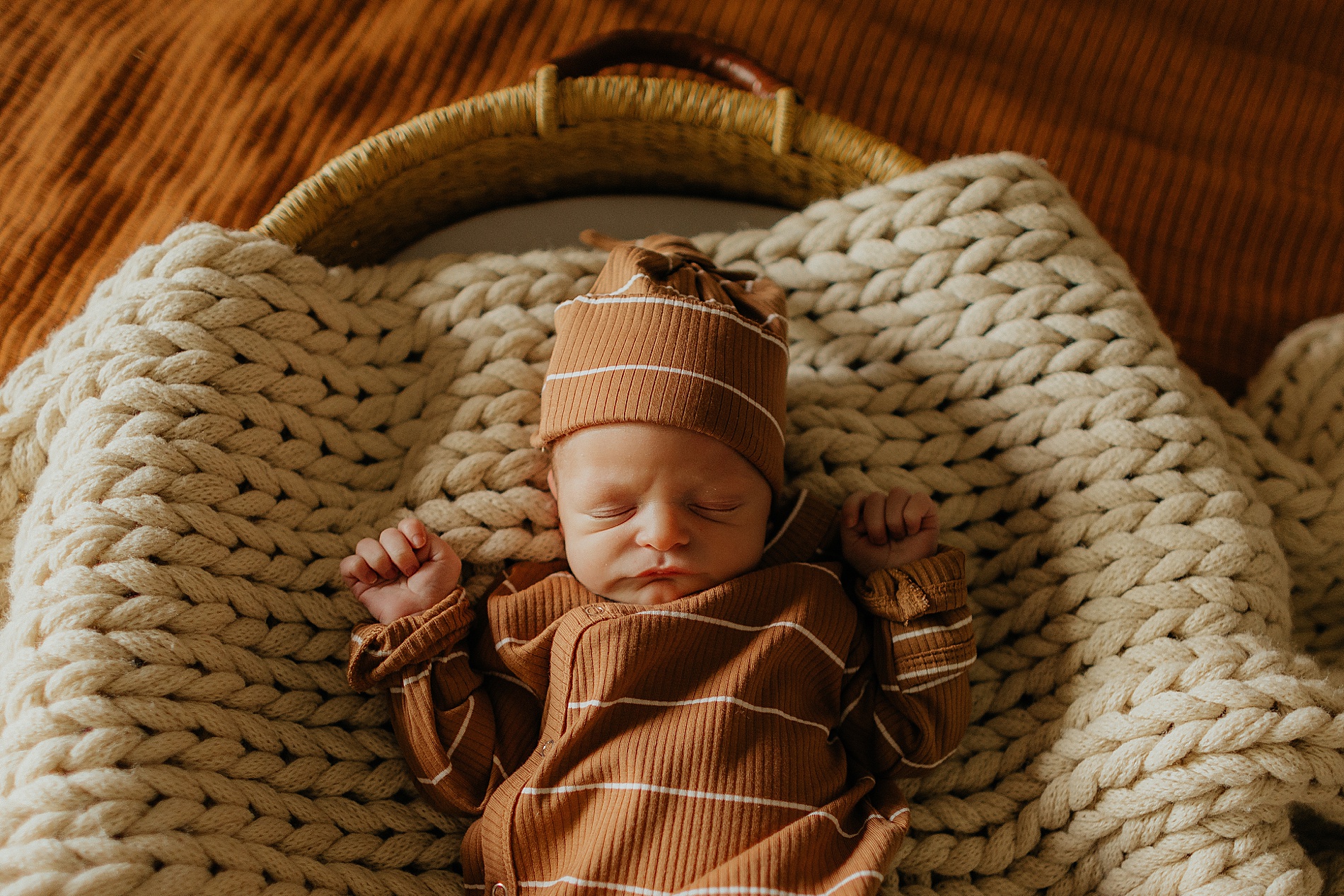 Newborn boy in striped onesie and hat lays in basket
