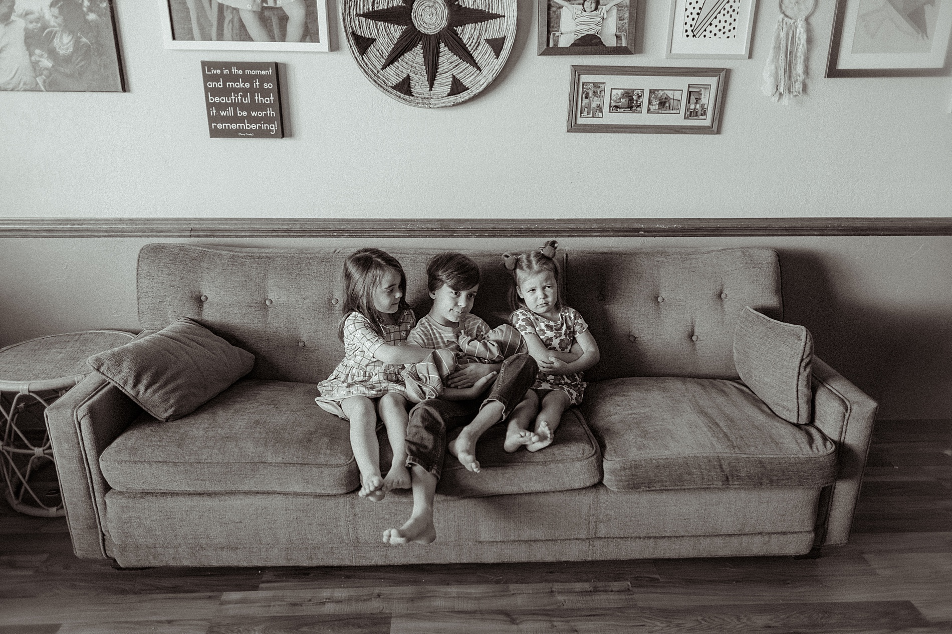 black and white photo of siblings sitting on couch holding their baby brother