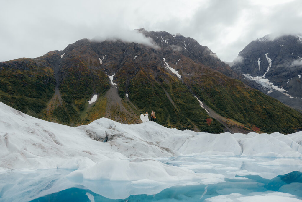 Bride and groom standing on Knik Glacier during a helicopter elopement in Alaska with blue glacial ice and mountain views.