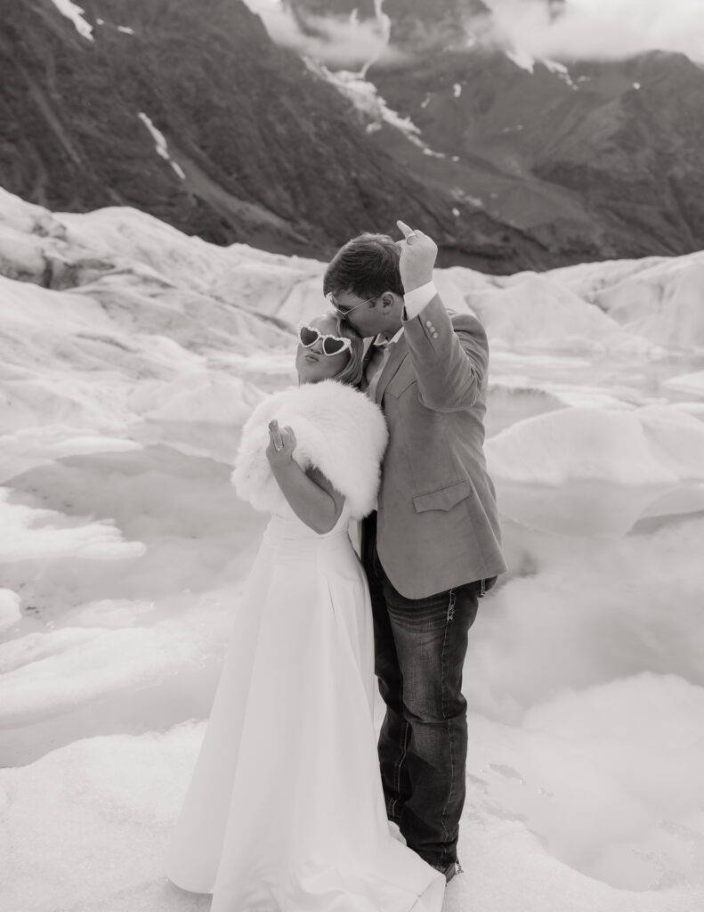 Bride and groom sharing a playful moment on Knik Glacier surrounded by snow, ice, and mountain views.