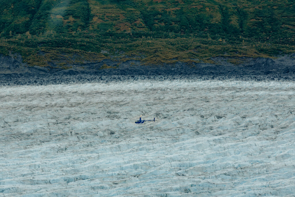 Helicopter landing on Knik Glacier surrounded by blue glacial ice in Alaska.