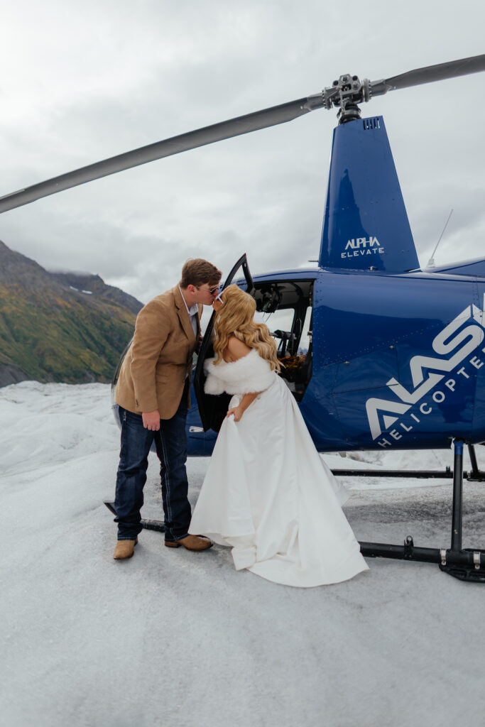 Bride and groom kissing beside their helicopter on Knik Glacier in Alaska.