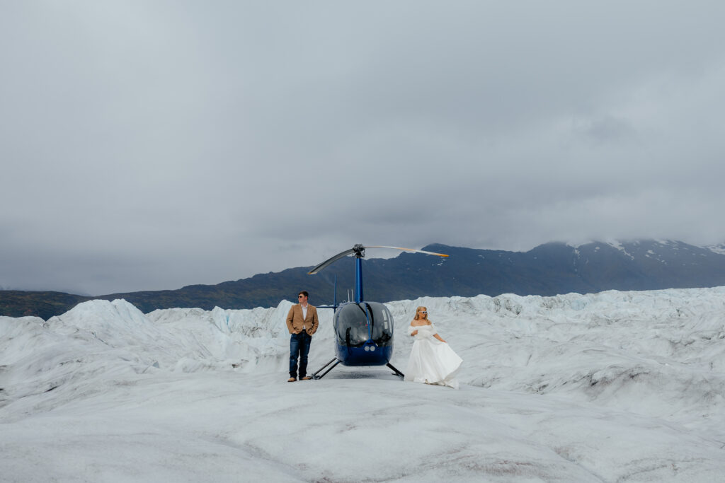 Bride and groom standing beside their helicopter on Knik Glacier in Alaska.