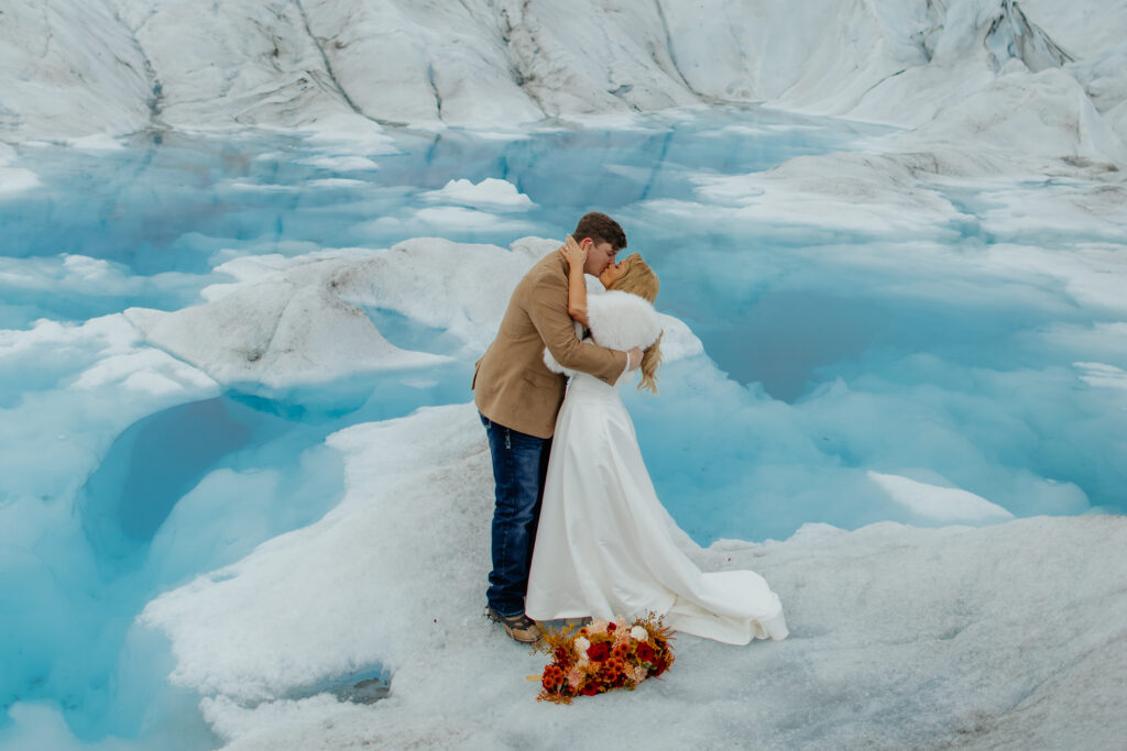 Newlyweds sharing a kiss on Knik Glacier after their helicopter elopement in Alaska.