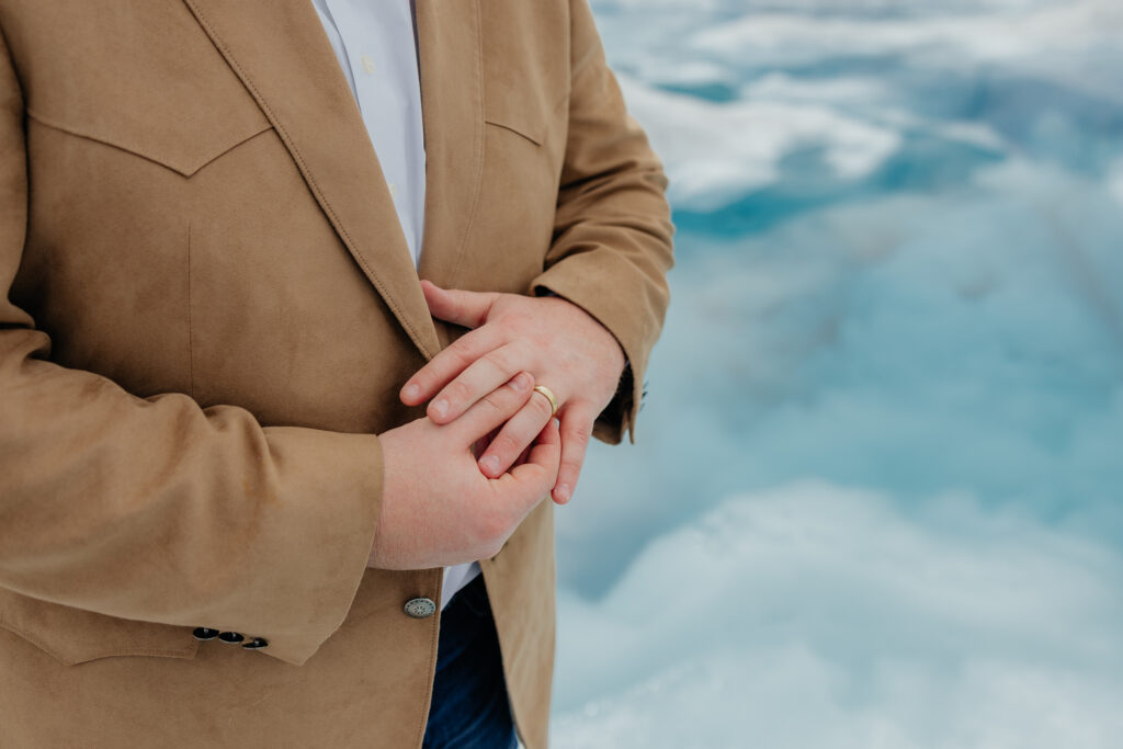 Close-up of the groom's gold wedding band with blue glacial ice in the background.
