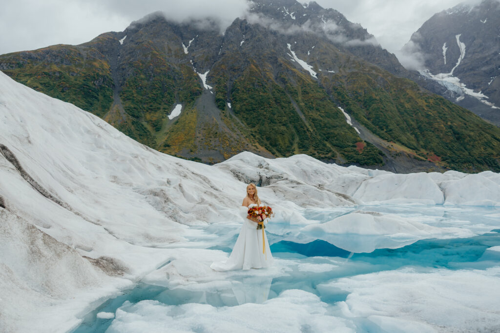 Bride holding her bouquet beside bright blue melt pools on Knik Glacier in Alaska.