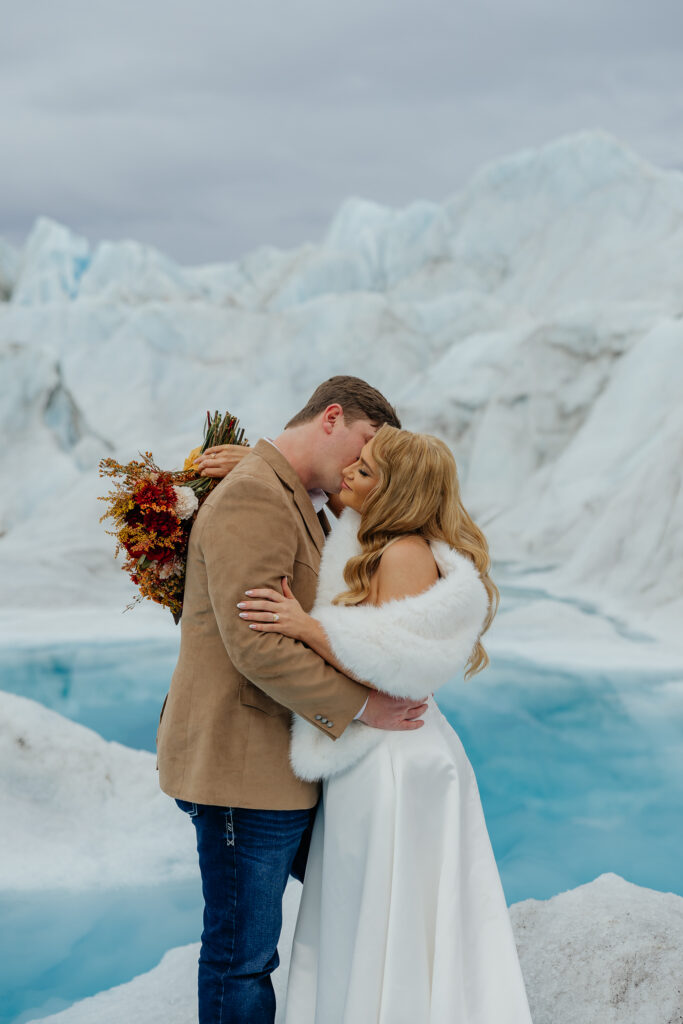 Bride and groom embracing on Knik Glacier surrounded by blue ice and towering glacier walls.