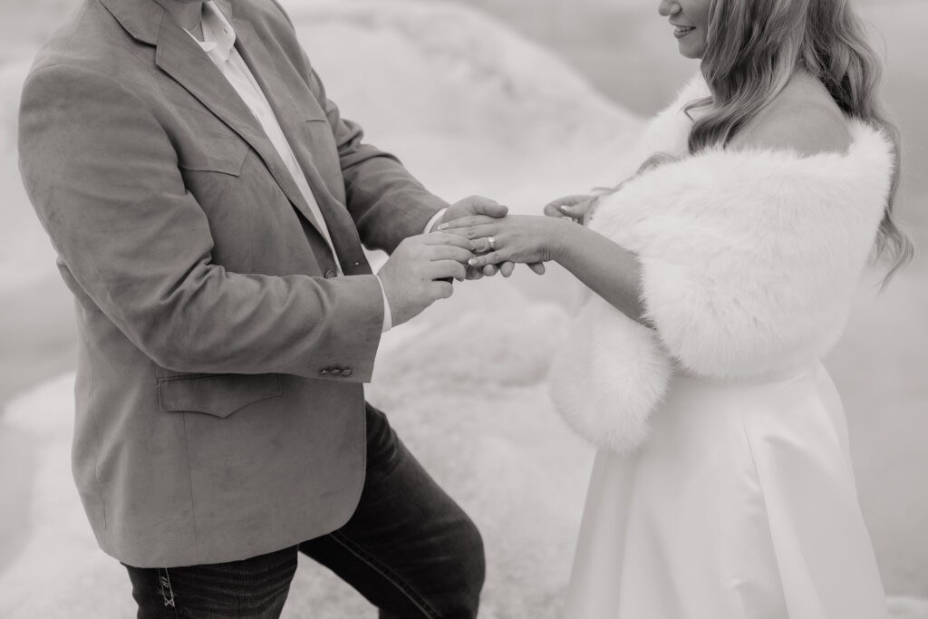 Groom placing a wedding ring on the bride's finger during their glacier ceremony in Alaska.