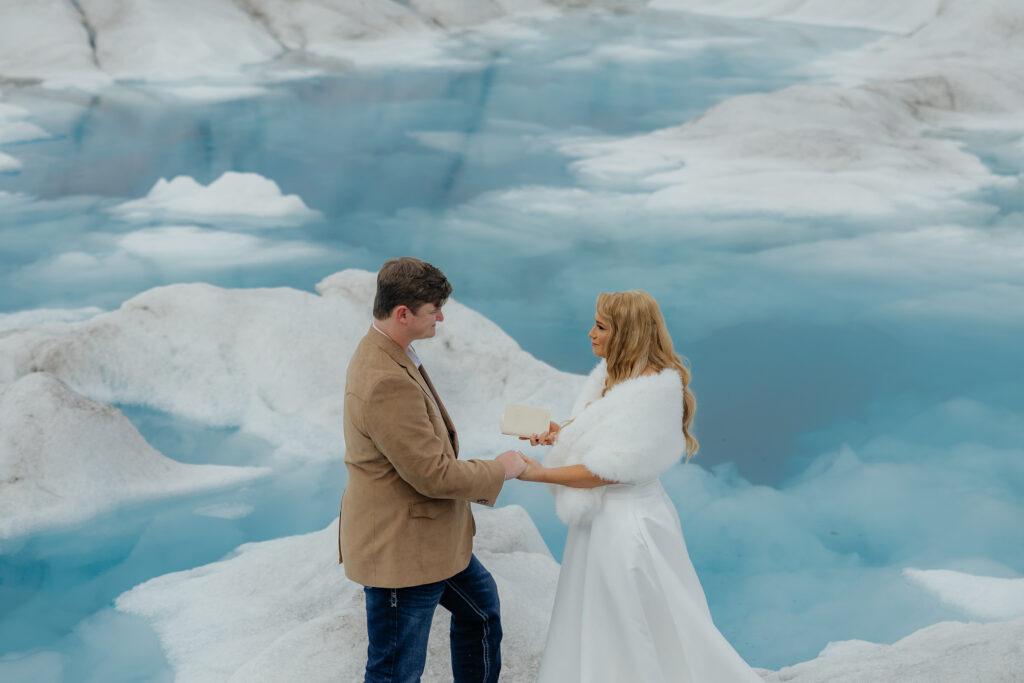 Couple holding hands while exchanging vows on Knik Glacier surrounded by blue glacial ice.