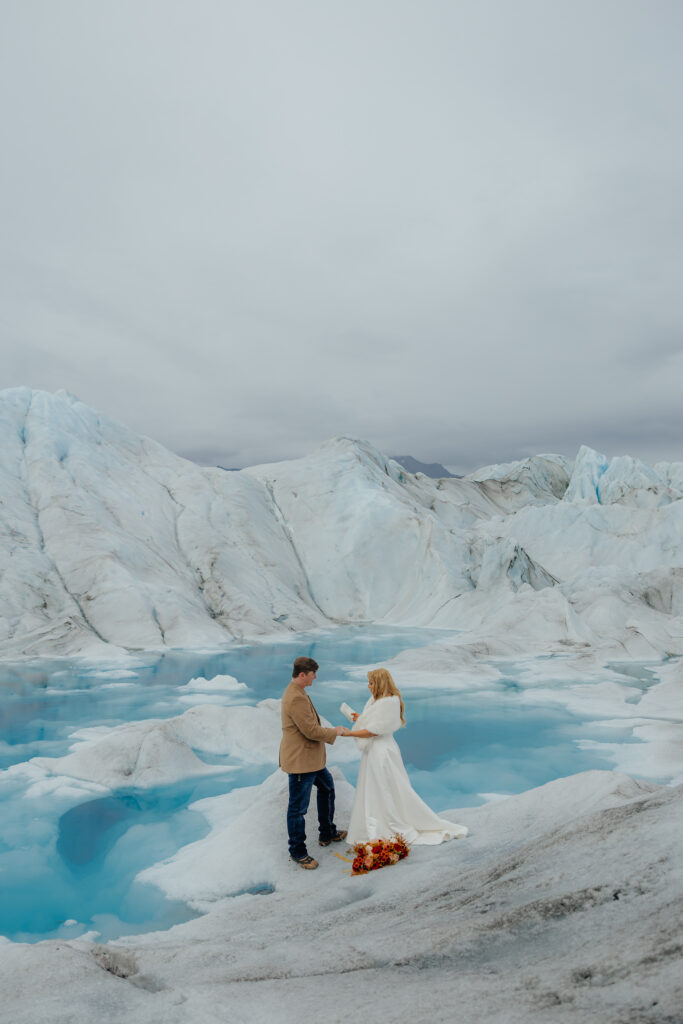 Bride and groom standing together on Knik Glacier surrounded by turquoise melt pools.