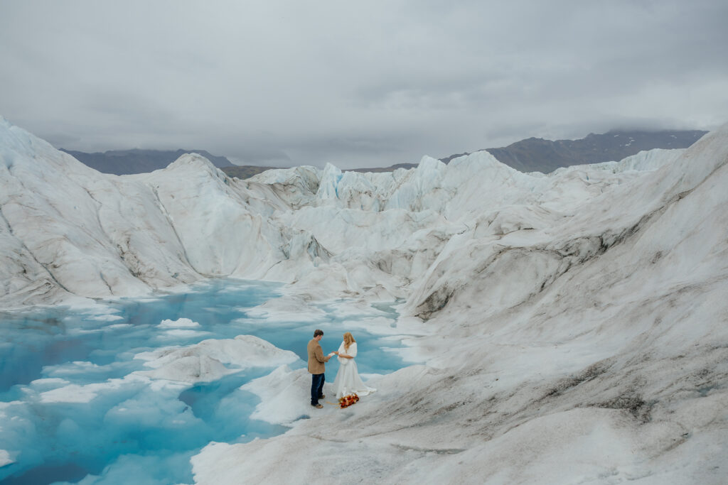 Bride and groom exchanging vows beside bright blue melt pools on Knik Glacier in Alaska.