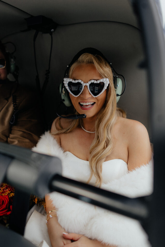 Bride wearing heart-shaped sunglasses inside the helicopter after her Alaska wedding.