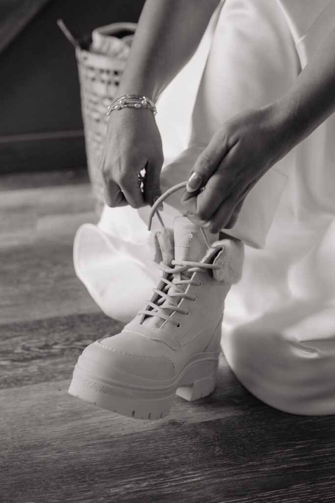 Bride lacing up white wedding boots before her Knik Glacier helicopter elopement.