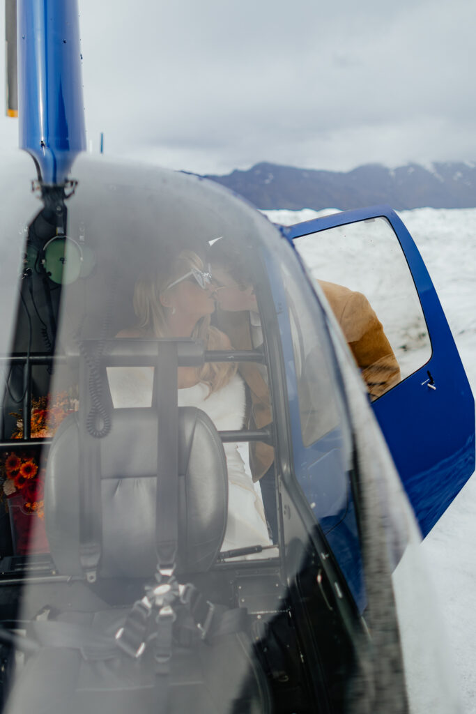 Bride and groom kiss while boarding the helicopter after their glacier wedding in Alaska.