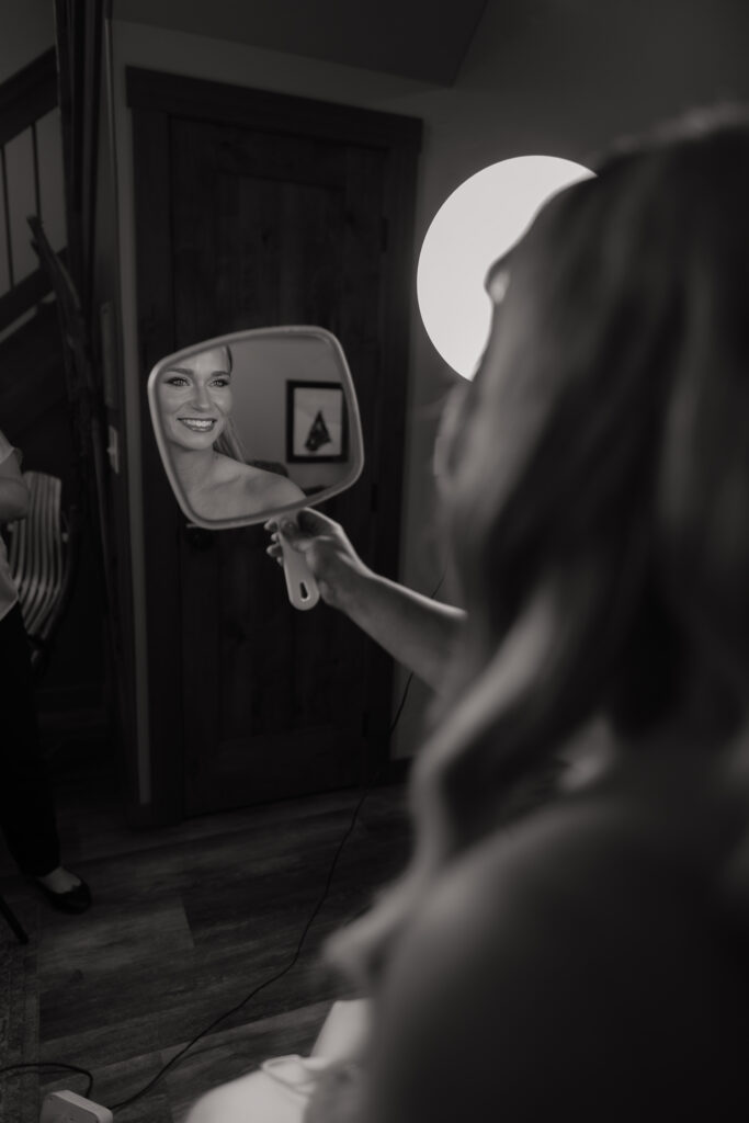 Bride checking her makeup in a hand mirror while getting ready for her Alaska helicopter elopement.
