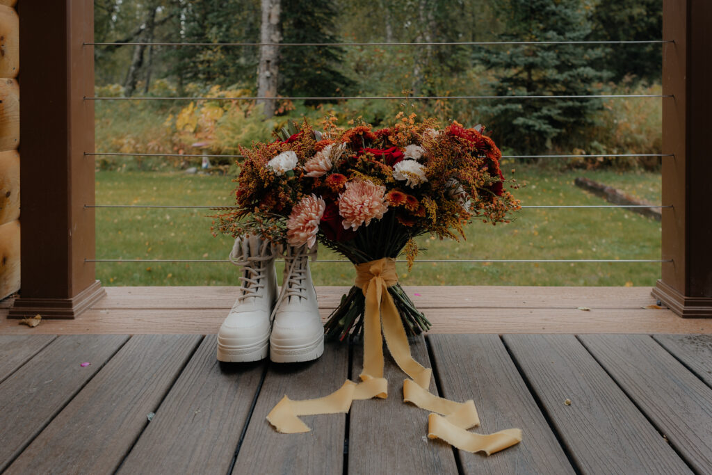 Bridal bouquet and white wedding boots on the porch before a Knik Glacier helicopter elopement in Alaska.
